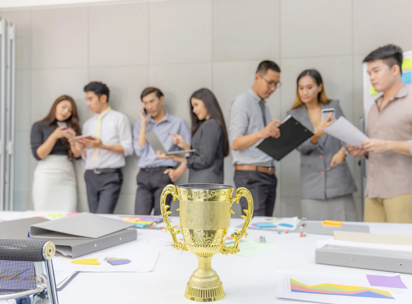 A trophy on a meeting table with colleagues conferring behind it